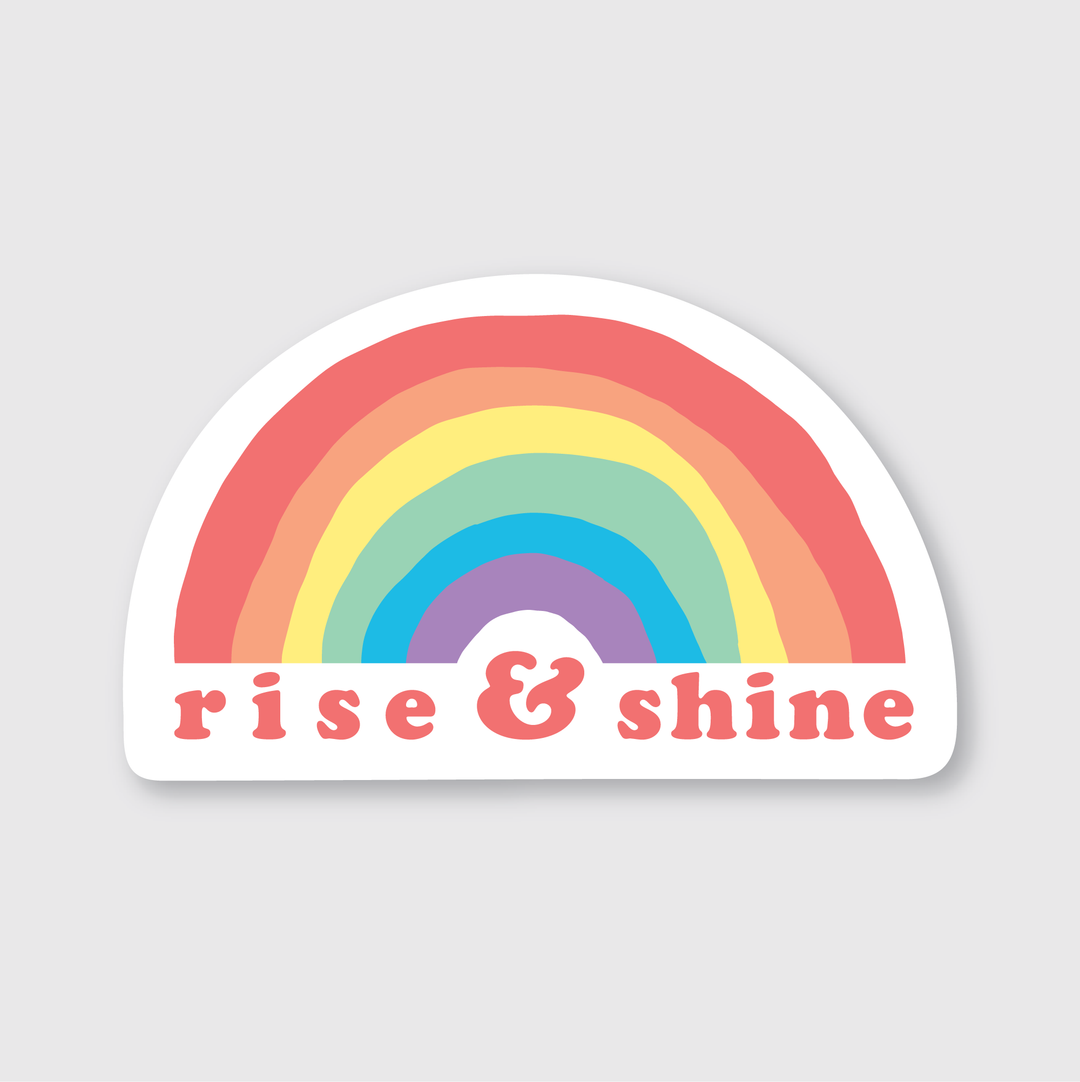 The Rainbow Sticker features a pastel rainbow arching over the words "rise & shine" in pink, set against a light gray background, and is of excellent quality.