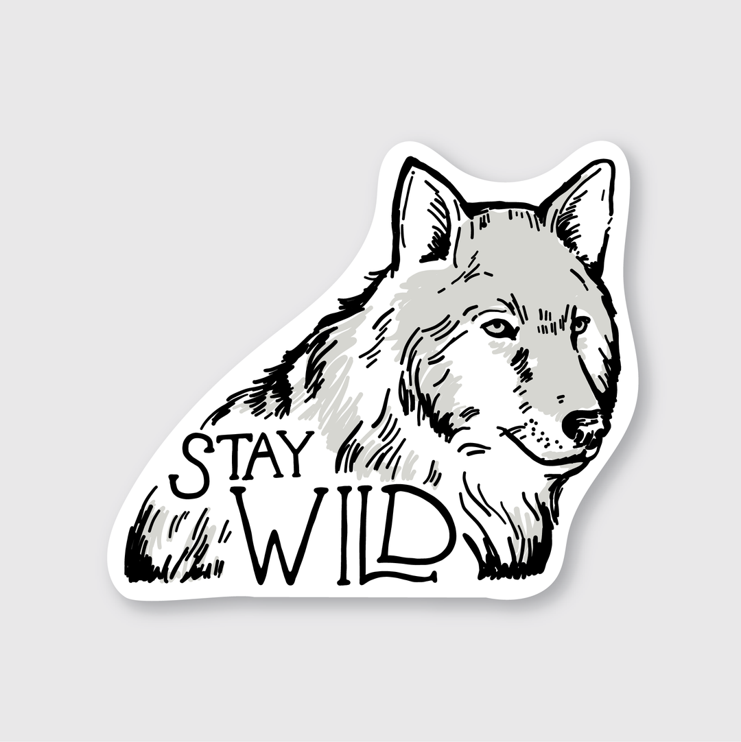 The Wolf Stay Wild Sticker showcases an illustration of a wolf with the phrase "Stay Wild" beneath it. The design is crafted in black and gray shades against a white background, giving it the appearance of a vinyl sticker.